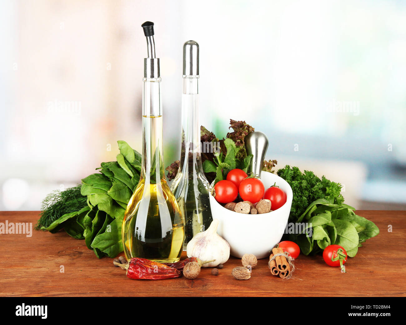 Composizione del mortaio, bottiglie con olio di oliva e aceto, e verde erboristeria, su sfondo lucido Foto Stock