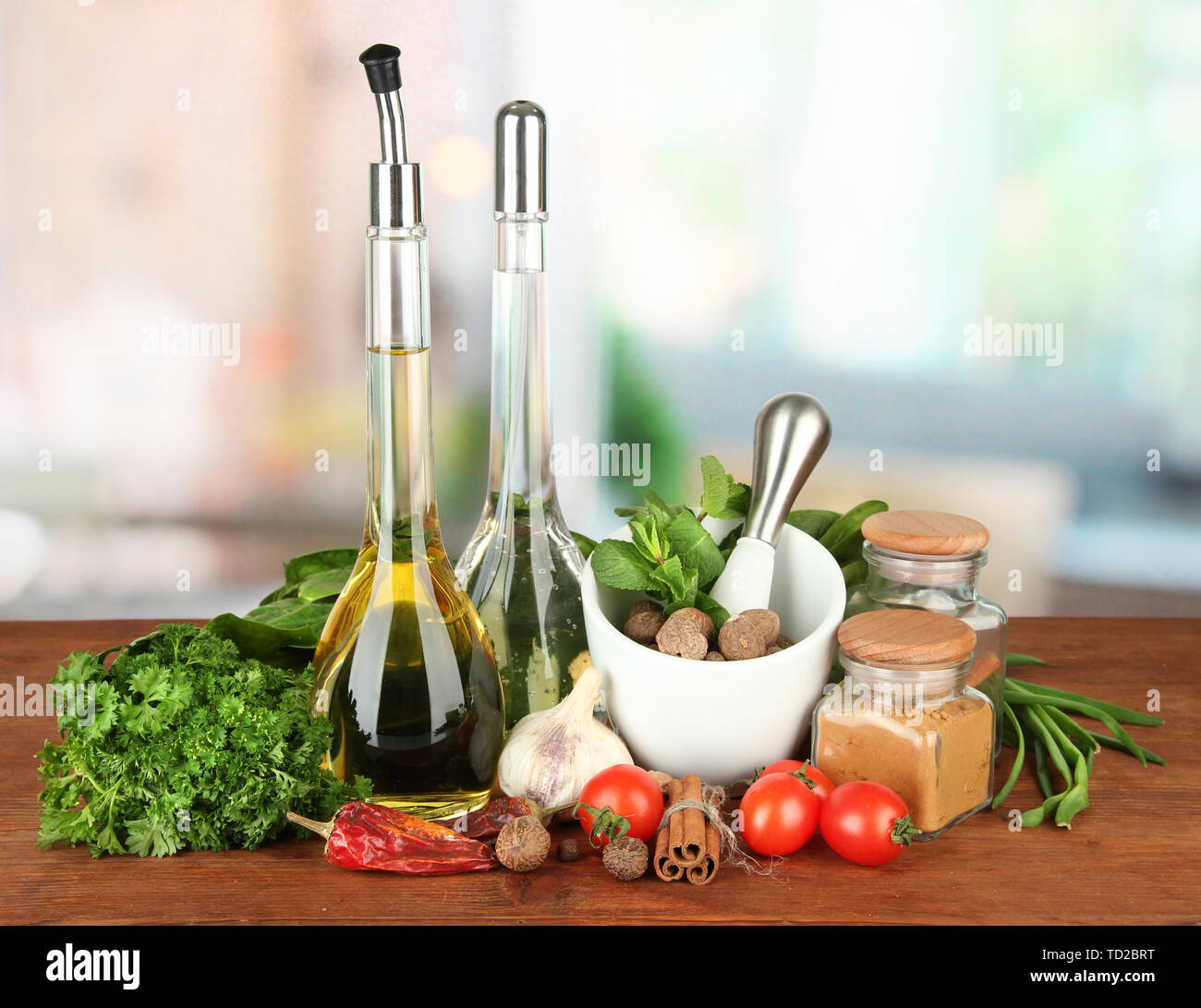 Composizione del mortaio, bottiglie con olio di oliva e aceto, e verde erboristeria, su sfondo lucido Foto Stock