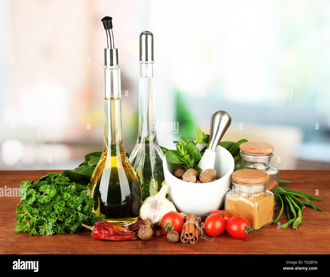 Composizione del mortaio, bottiglie con olio di oliva e aceto, e verde erboristeria, su sfondo lucido Foto Stock