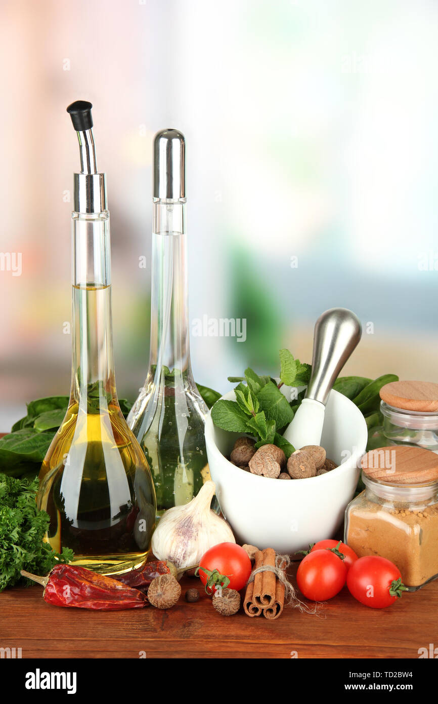 Composizione del mortaio, bottiglie con olio di oliva e aceto, e verde erboristeria, su sfondo lucido Foto Stock