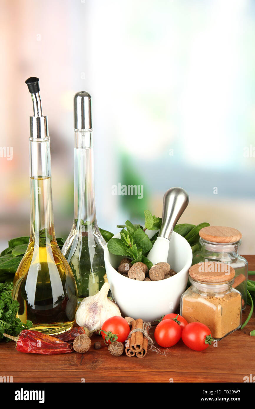 Composizione del mortaio, bottiglie con olio di oliva e aceto, e verde erboristeria, su sfondo lucido Foto Stock