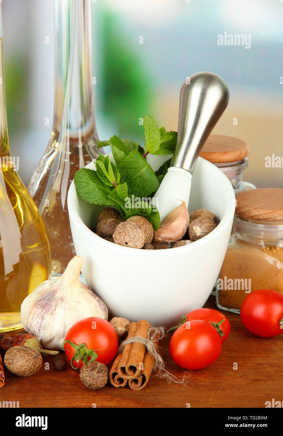 Composizione del mortaio, bottiglie con olio di oliva e aceto, e verde erboristeria, su sfondo lucido Foto Stock