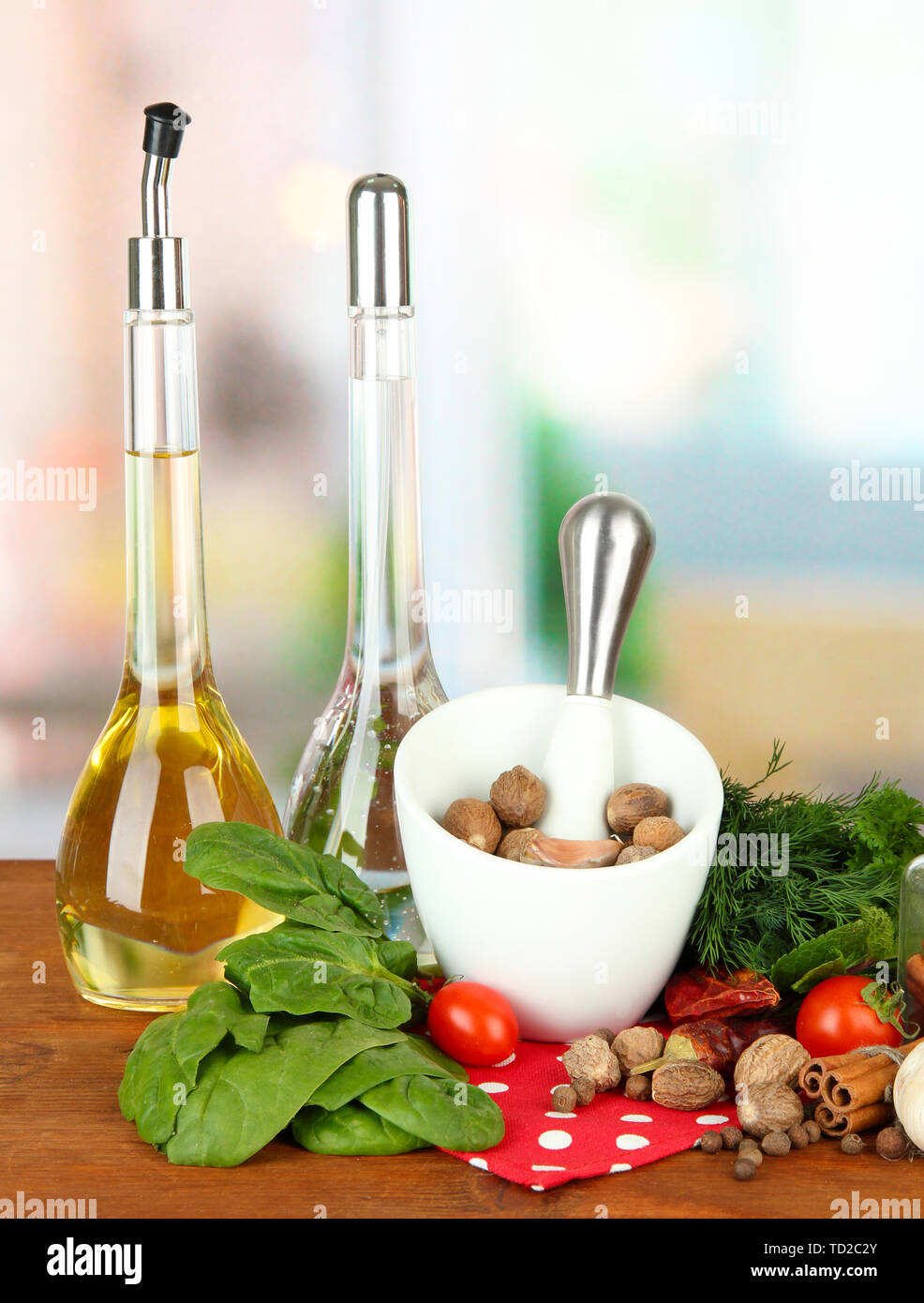 Composizione del mortaio, bottiglie con olio di oliva e aceto, e verde erboristeria, su sfondo lucido Foto Stock