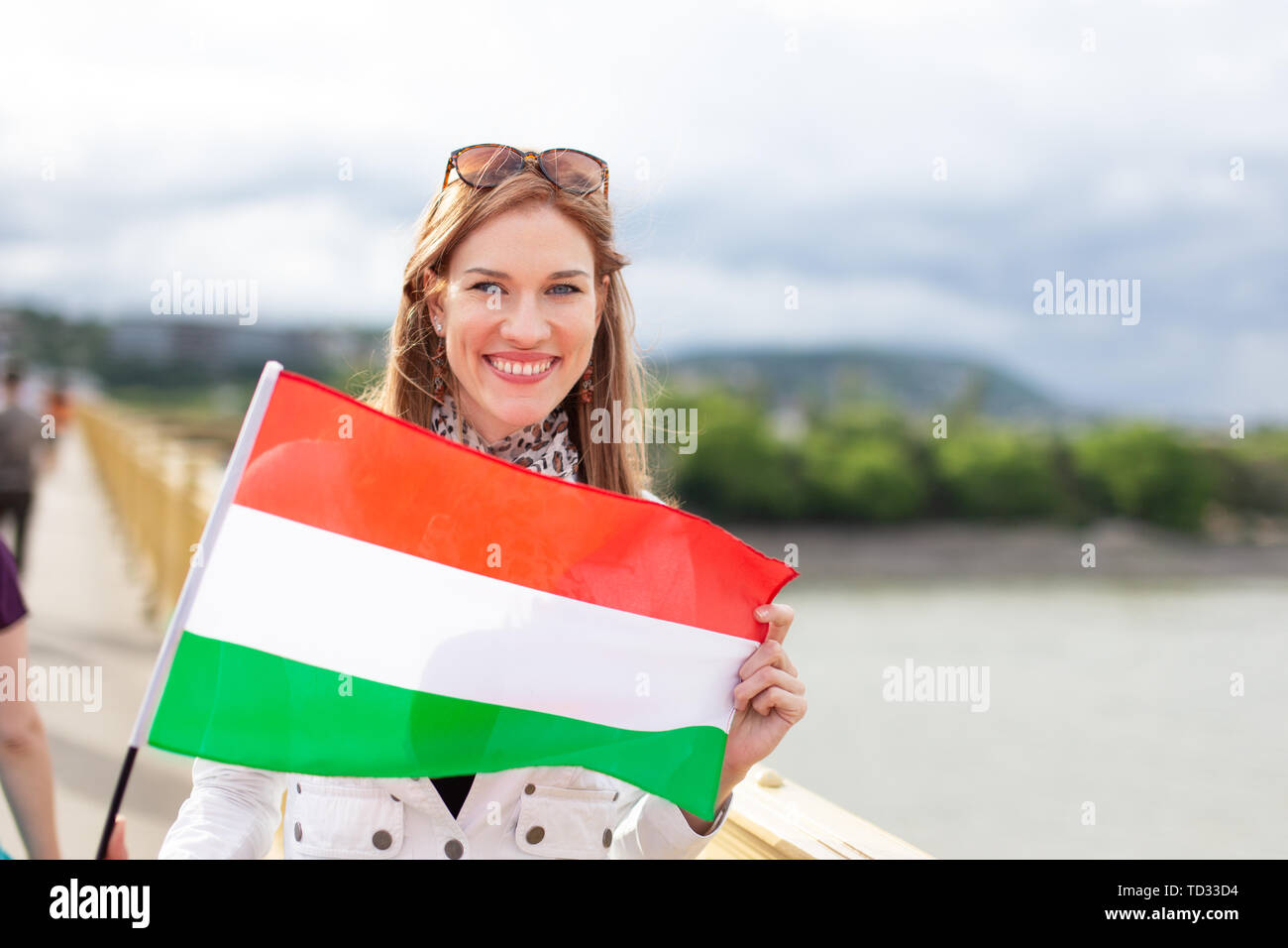 Felice giovane bellezza naturale donna holding bandiera di Ungheria con sorriso toothy, all'aperto in città, Budapest, Ungheria Foto Stock