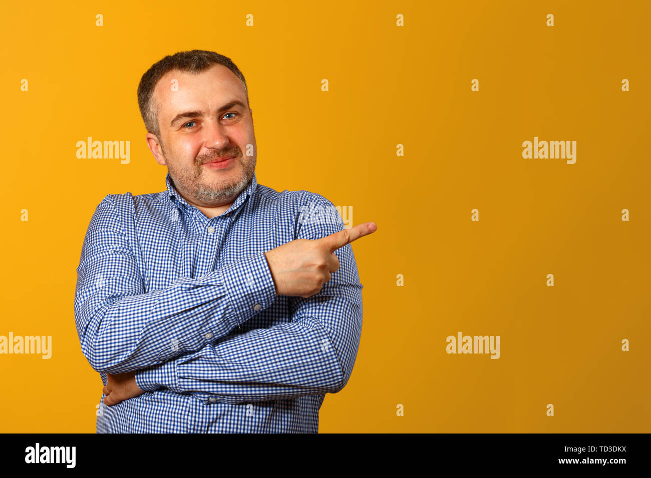 Bel uomo barbuto in una camicia, punta il dito sul lato, guarda nella telecamera e sorrisi, contro uno sfondo giallo. Copia dello spazio. Close-up. Foto Stock