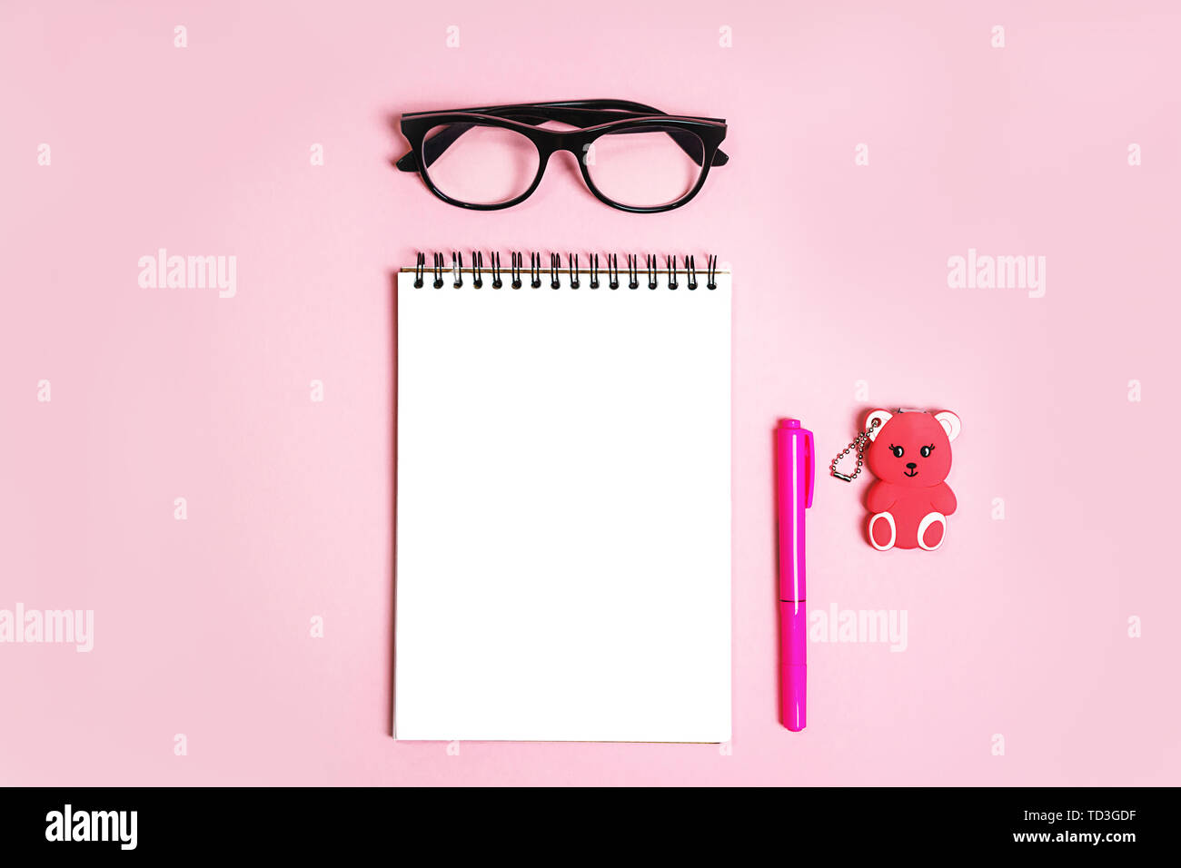 Blocco note con occhiali trendy e corallo rosa penna e orso giocattolo regalo pastello su sfondo rosa. Foto Stock