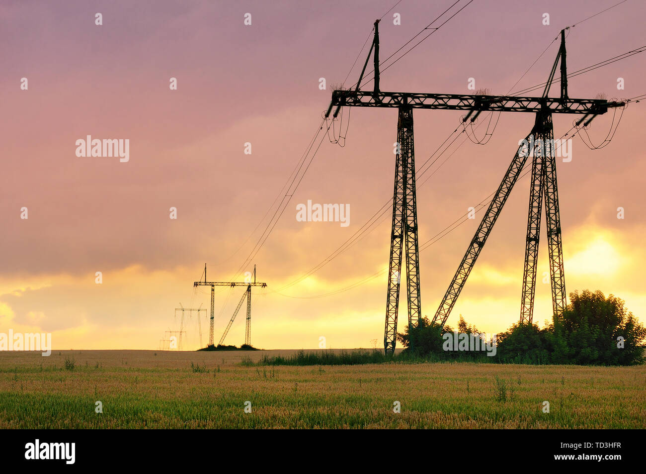 Linea elettrica di alimentazione nel campo coltivato contro vivid Cielo di tramonto Foto Stock