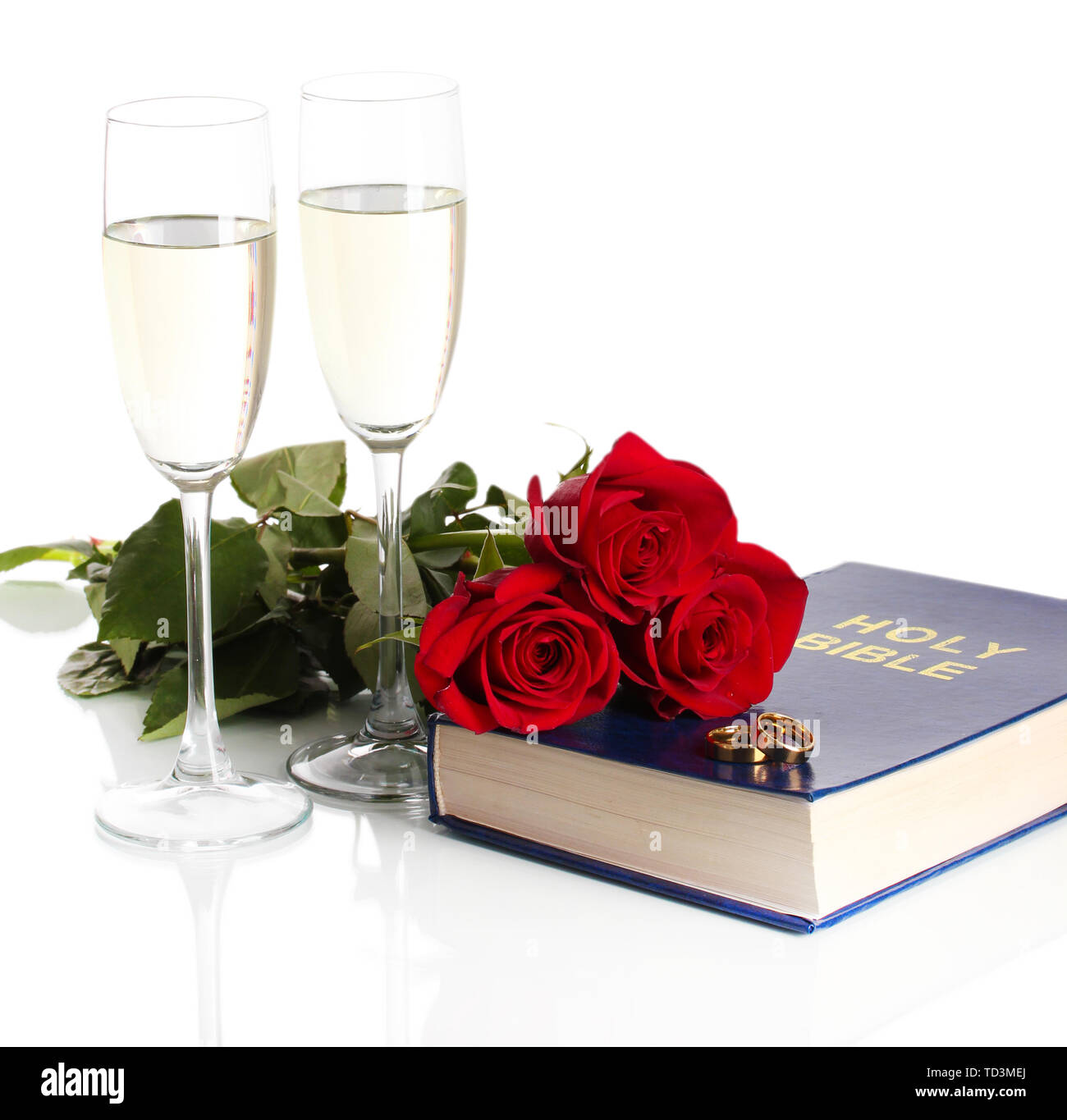 Gli anelli di nozze sulla bibbia con rose e bicchieri di champagne isolato su bianco Foto Stock