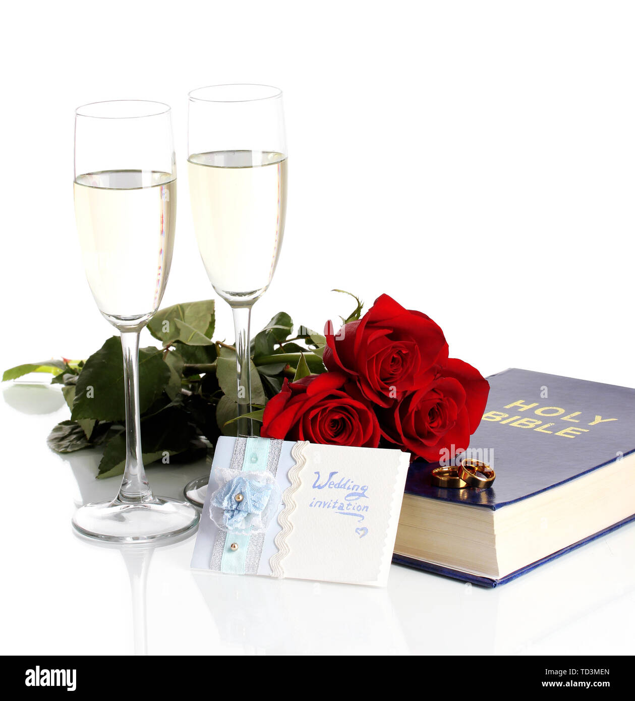 Gli anelli di nozze sulla bibbia con rose e bicchieri di champagne isolato su bianco Foto Stock