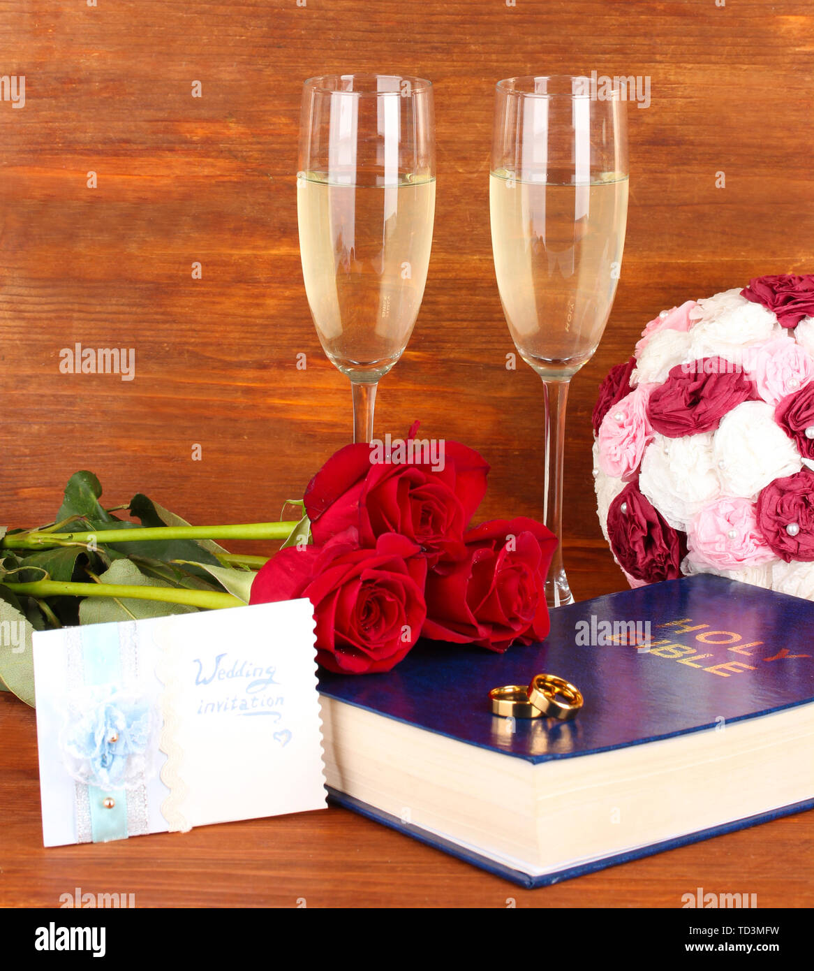 Gli anelli di nozze sulla bibbia con rose e bicchieri di champagne su sfondo di legno Foto Stock