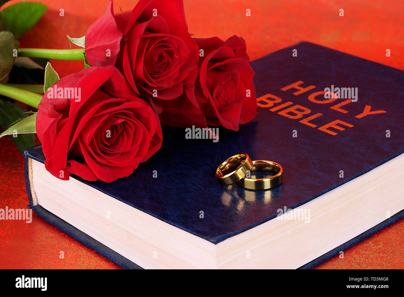 Gli anelli di nozze con rose sulla Bibbia su sfondo rosso Foto Stock
