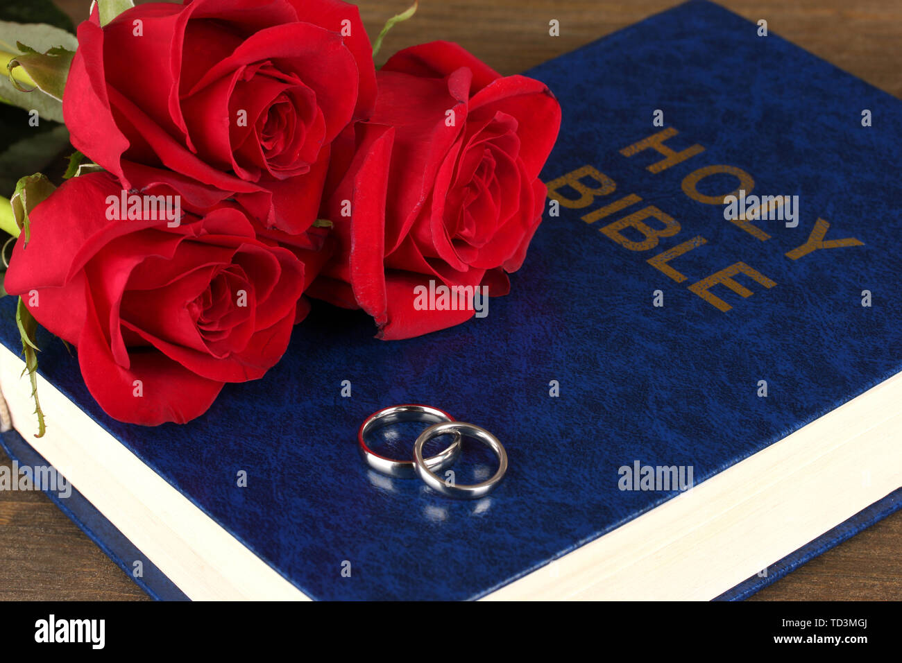 Gli anelli di nozze sulla bibbia con rose su sfondo di legno Foto Stock