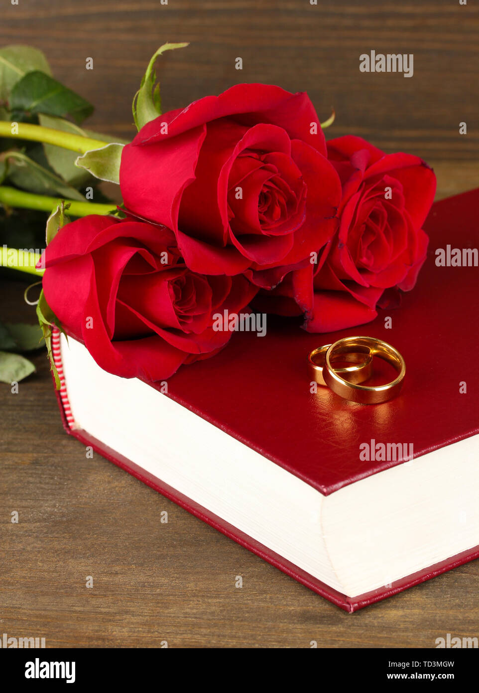 Gli anelli di nozze sulla bibbia con rose su sfondo di legno Foto Stock