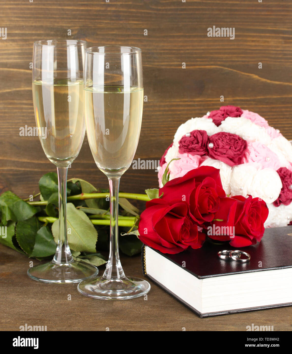 Gli anelli di nozze sulla bibbia con rose e bicchieri di champagne su sfondo di legno Foto Stock