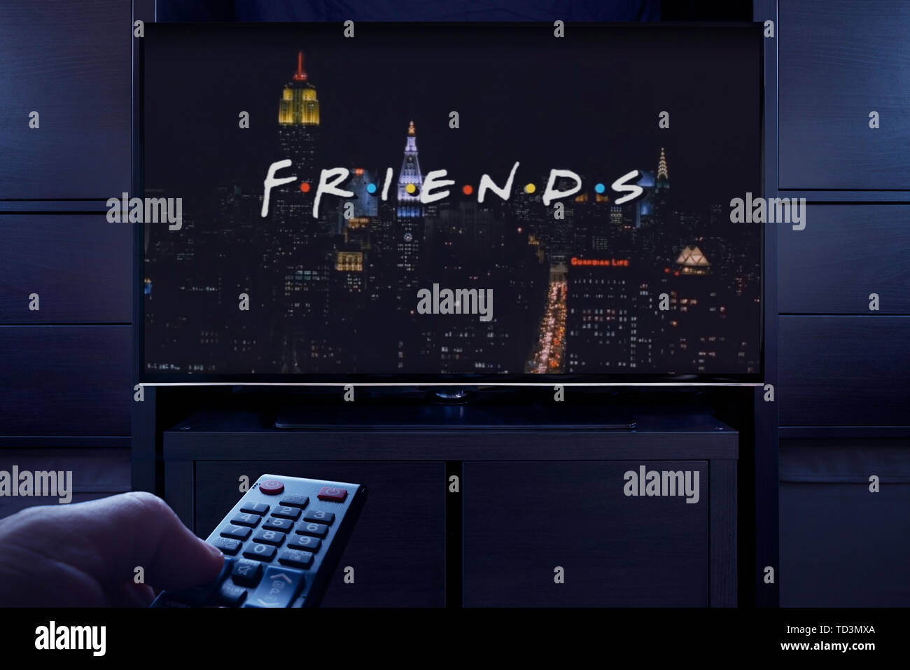 Un uomo punti un telecomando TV al televisore che visualizza gli amici titolo principale schermo (solo uso editoriale). Foto Stock