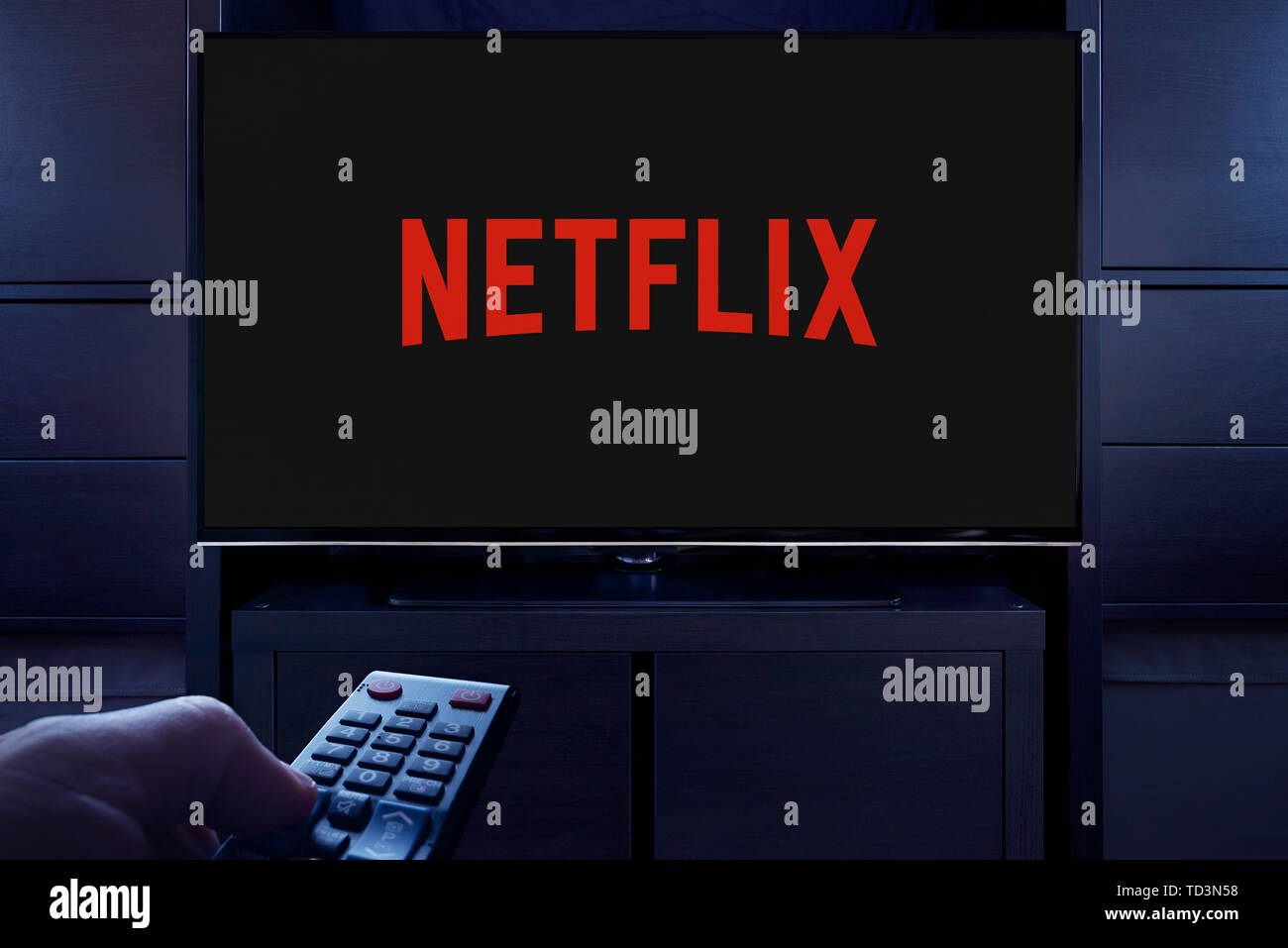 Un uomo punti un telecomando TV al televisore che visualizza il logo per il Netflix on demand video streaming service (solo uso editoriale). Foto Stock