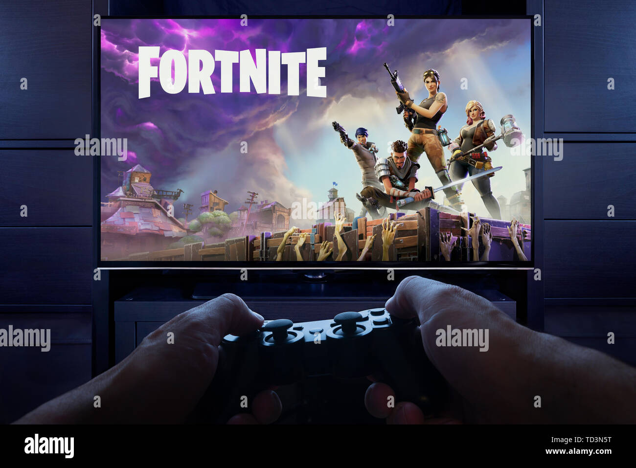 Con controller di Playstation in mano, un uomo si prepara a riprodurre Fortnite: salvare il mondo come intro e la schermata di caricamento in visto su una TV (solo uso editoriale). Foto Stock