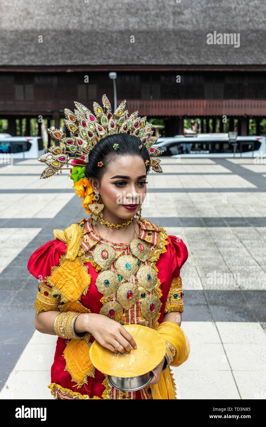 Makassar, Sulawesi, Indonesia - 28 Febbraio 2019: primo piano della giovane donna nel tradizionale abito locale. Rossi e Gialli contro di legno marrone scuro e palace Foto Stock