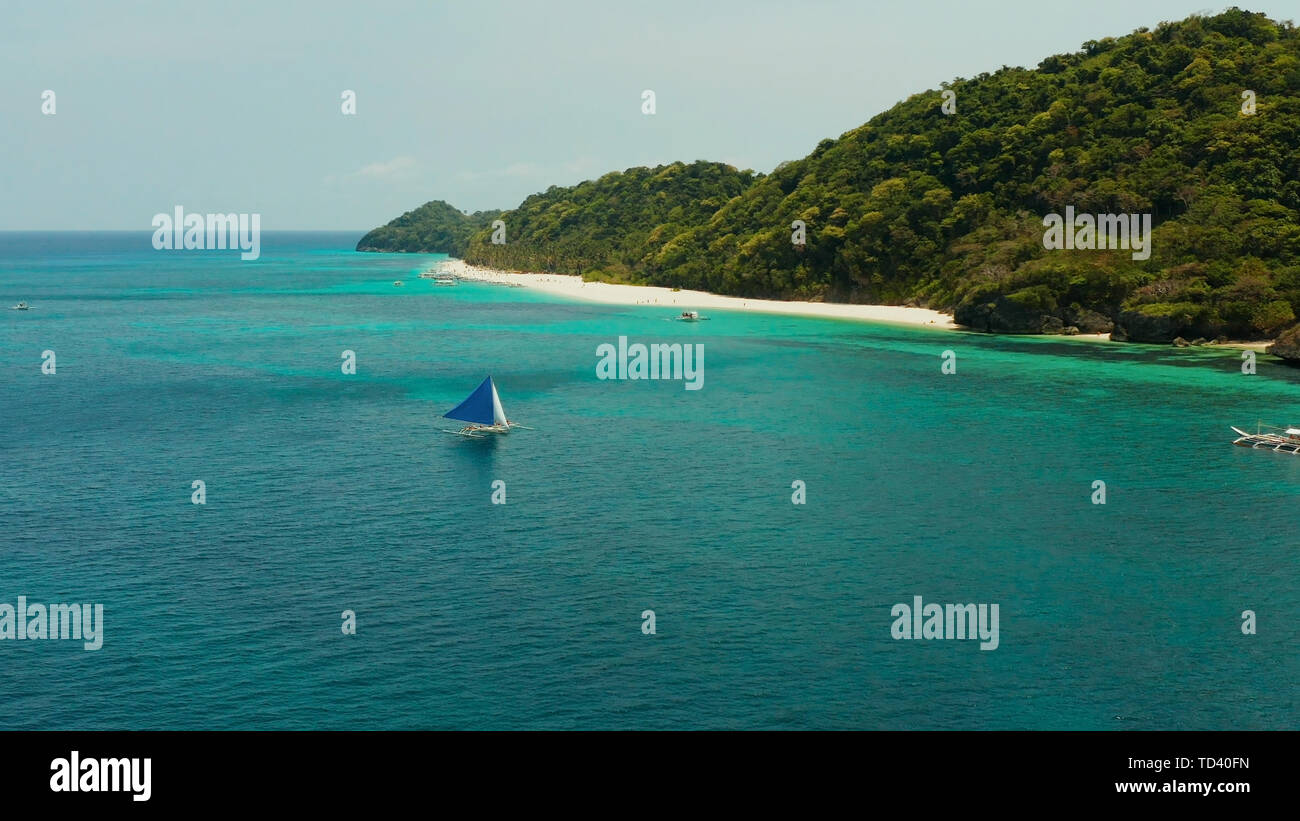 Sailing yacht in crystal turchesi acque cristalline proprio accanto alla spiaggia di sabbia bianca di isola tropicale, vista aerea. Barca a vela scivola sulle onde, Boracay, Filippine. Foto Stock