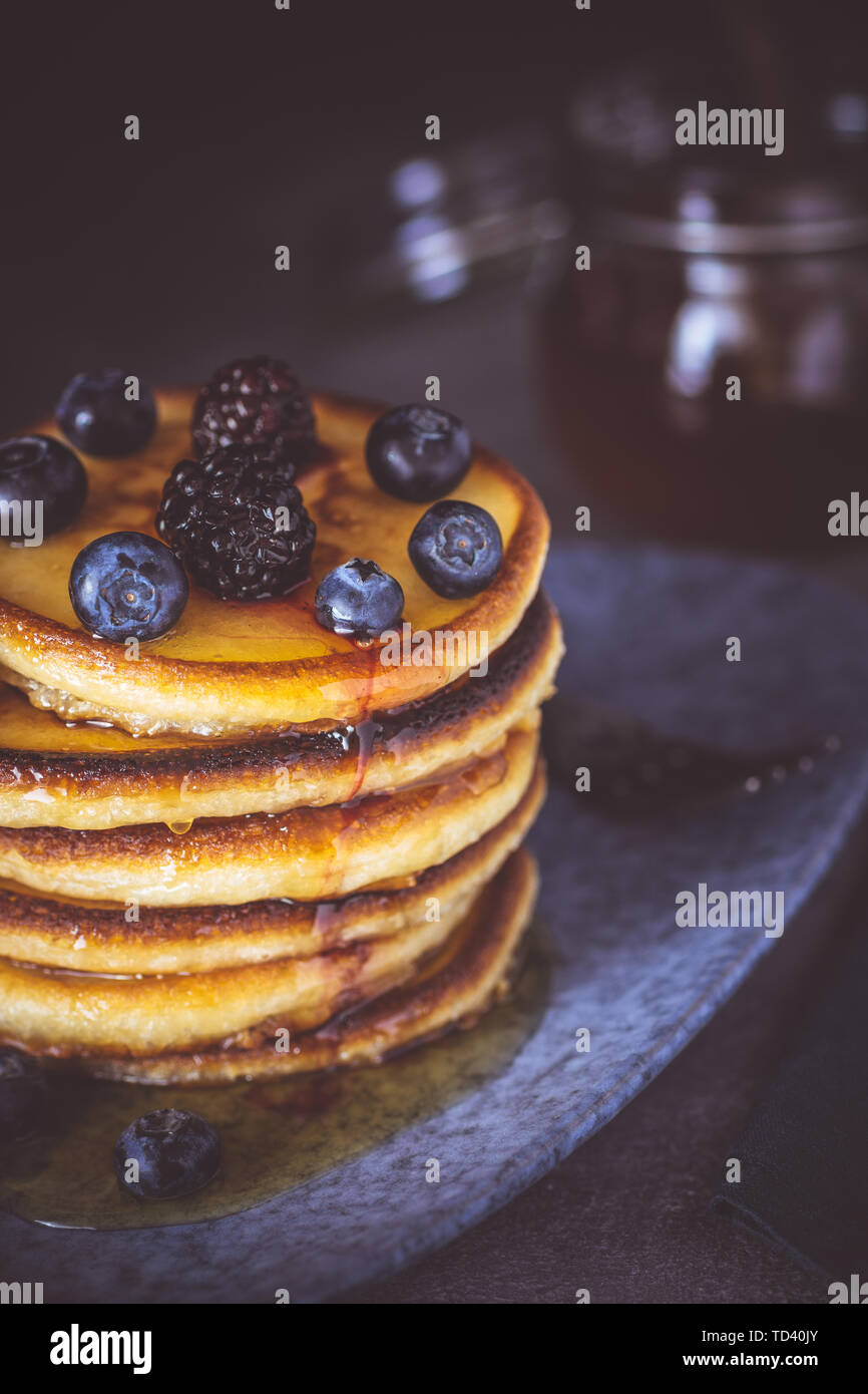 American pancake con bacche organiche e sciroppo d'acero sul Moody scuro dello sfondo. Classic colazione casalinga. Foto Stock