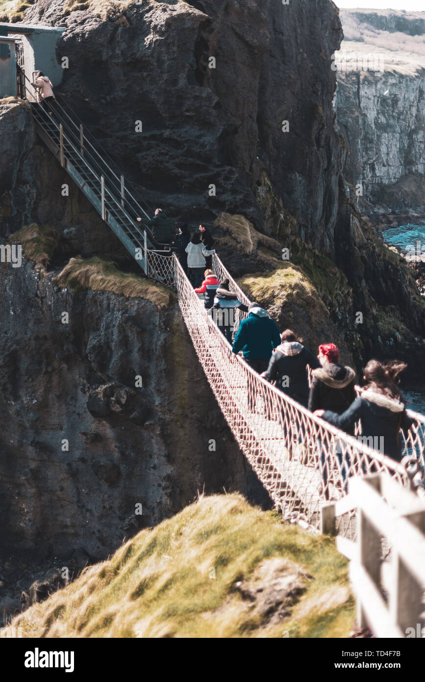 Irlanda del Nord, Regno Unito - 8° aprile 2019: spaventato i turisti attraversare il pericoloso ma bella Carrick-a-Rede ponte di corde Foto Stock