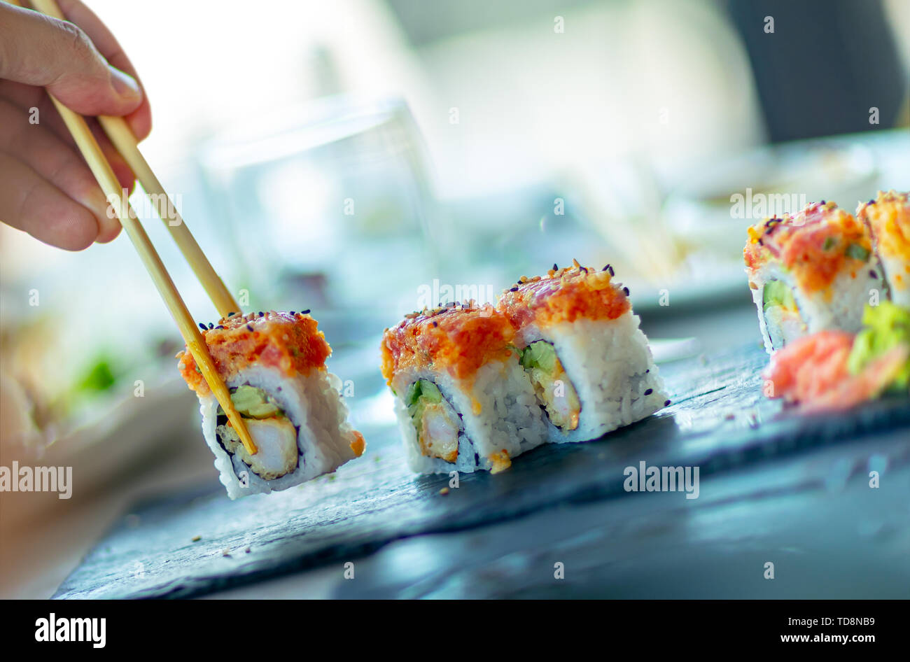 Un uomo in un ristorante asiatico, mangiare sushi con bacchette, trendy cibo orientale, cucina Giapponese tradizionale Foto Stock
