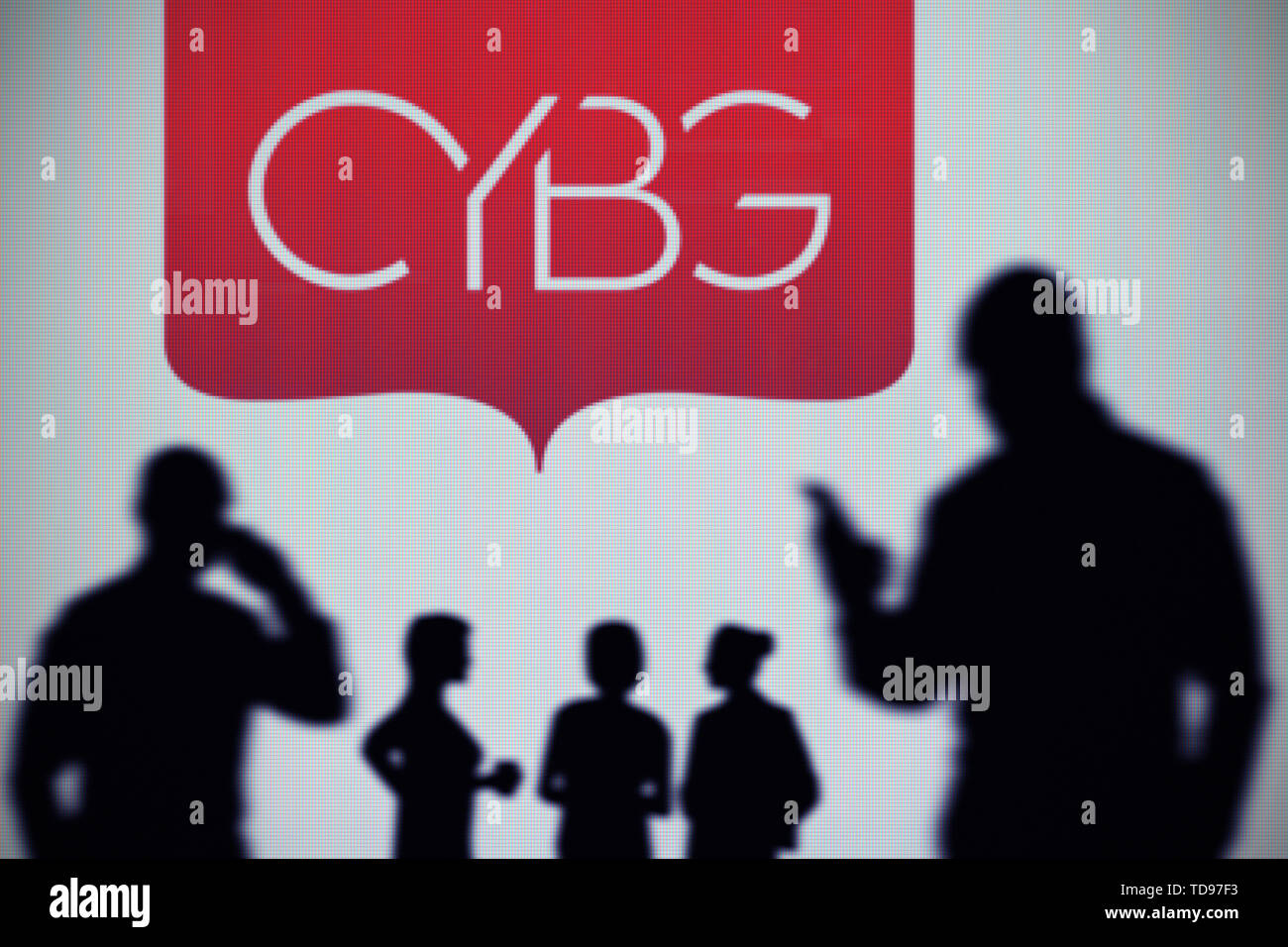 Il logo CYBG è visto su uno schermo a LED in background mentre si profila una persona utilizza uno smartphone in primo piano (solo uso editoriale) Foto Stock
