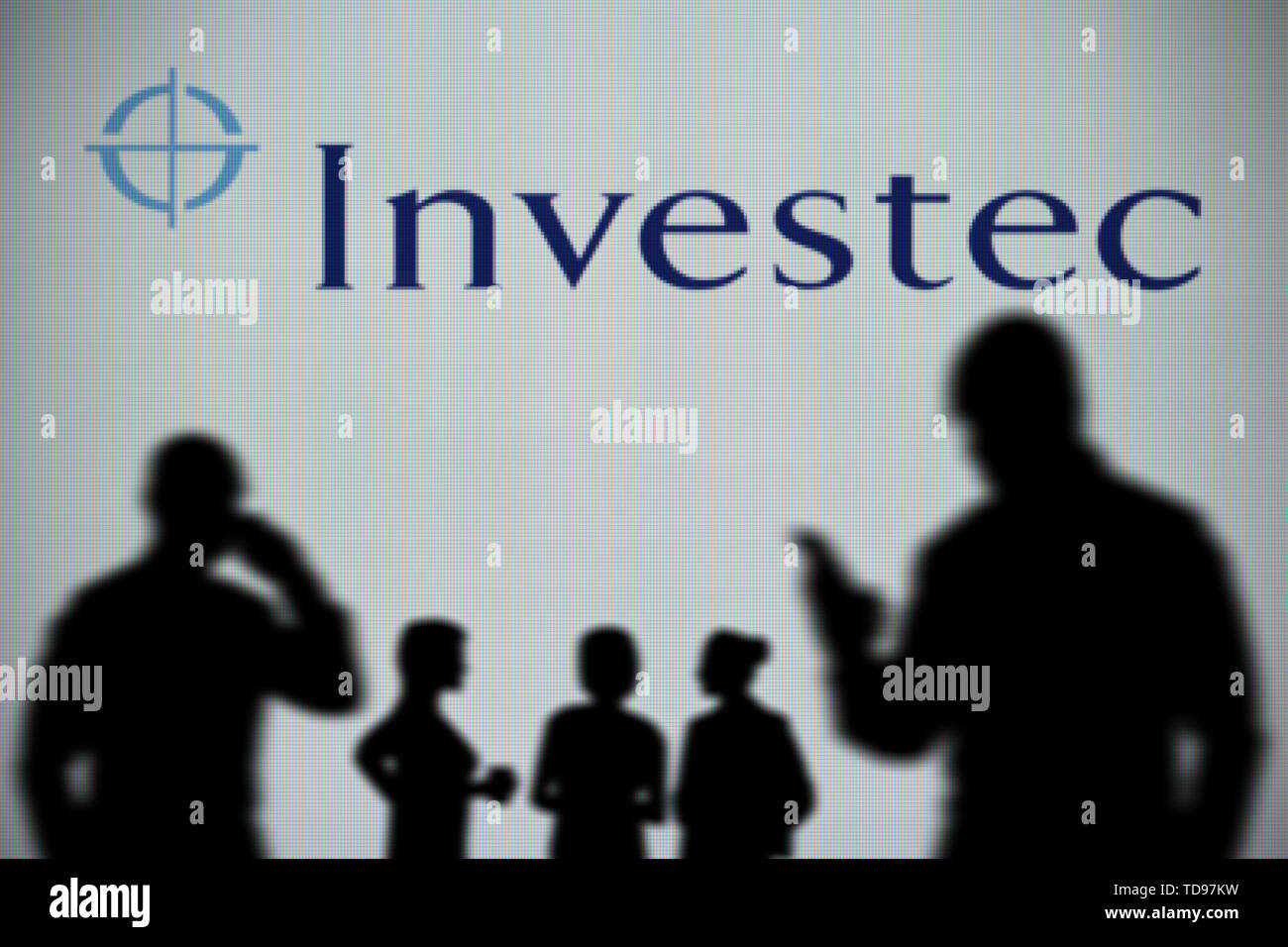 Il logo Investec è visto su uno schermo a LED in background mentre si profila una persona utilizza uno smartphone in primo piano (solo uso editoriale) Foto Stock