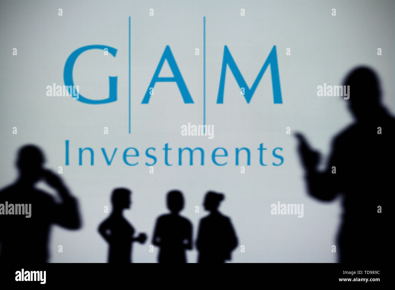 La GAM investimenti logo è visibile su uno schermo a LED in background mentre si profila una persona utilizza uno smartphone in primo piano (solo uso editoriale Foto Stock