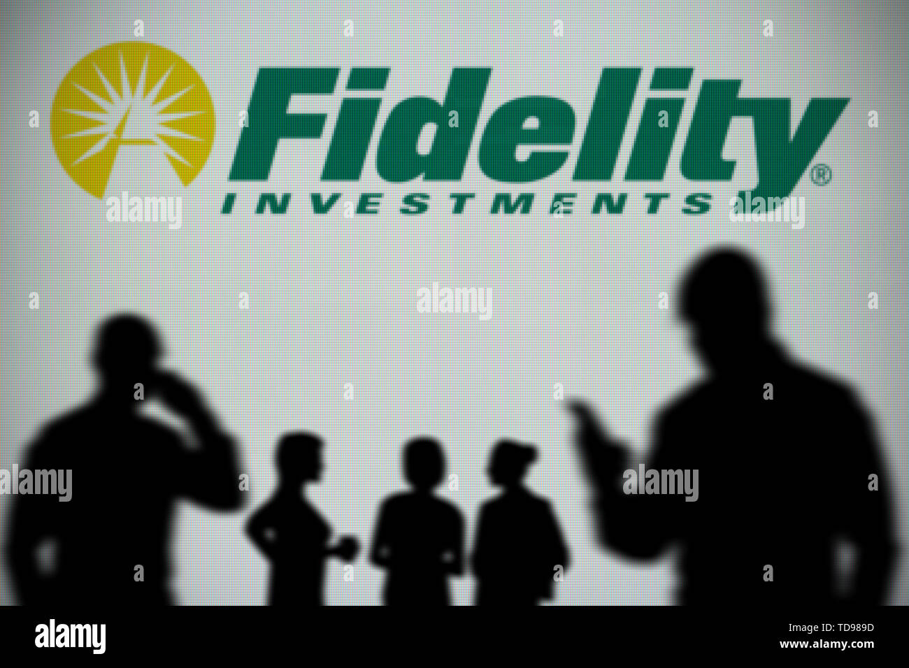 La Fidelity Investments logo è visibile su uno schermo a LED in background mentre si profila una persona utilizza uno smartphone (solo uso editoriale) Foto Stock