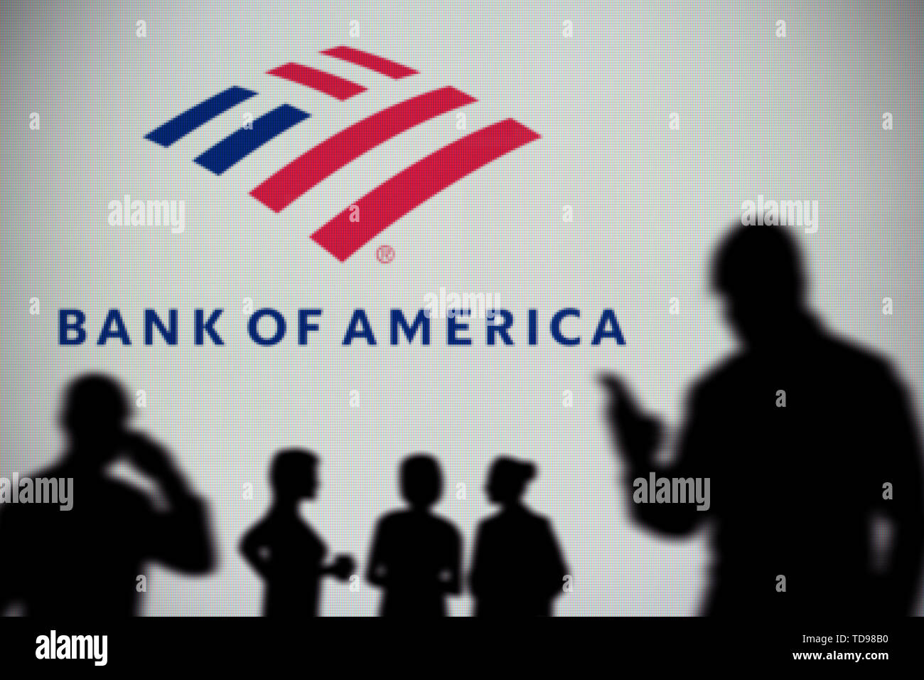 La Bank of America il logo è visibile su uno schermo a LED in background mentre si profila una persona utilizza uno smartphone in primo piano (solo uso editoriale Foto Stock