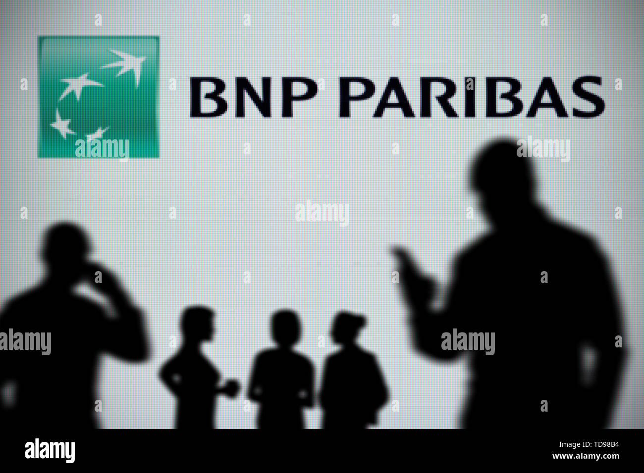 La BNP Paribas logo è visibile su uno schermo a LED in background mentre si profila una persona utilizza uno smartphone in primo piano (solo uso editoriale) Foto Stock