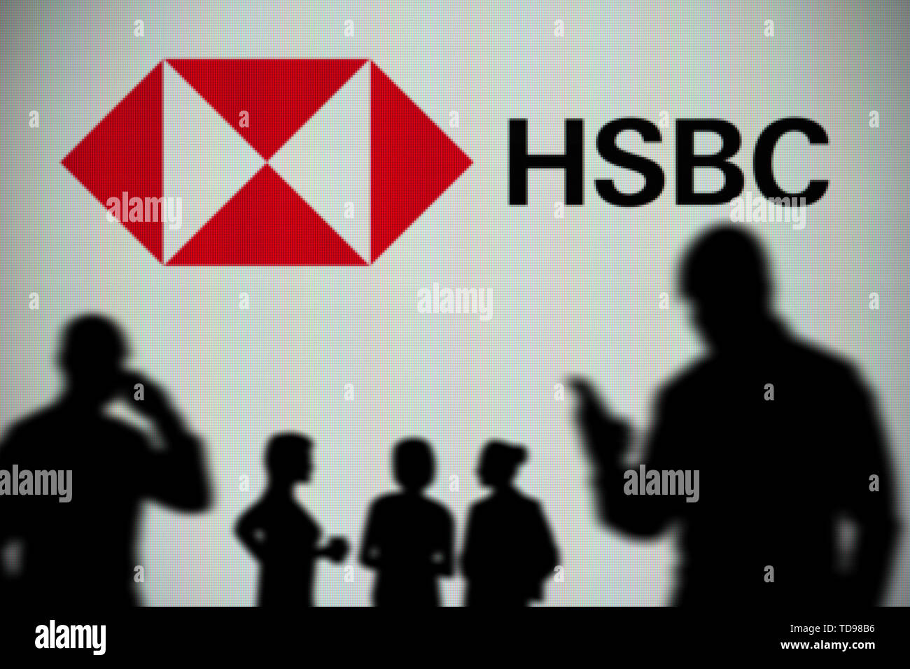 Il logo di HSBC è visto su uno schermo a LED in background mentre si profila una persona utilizza uno smartphone in primo piano (solo uso editoriale) Foto Stock