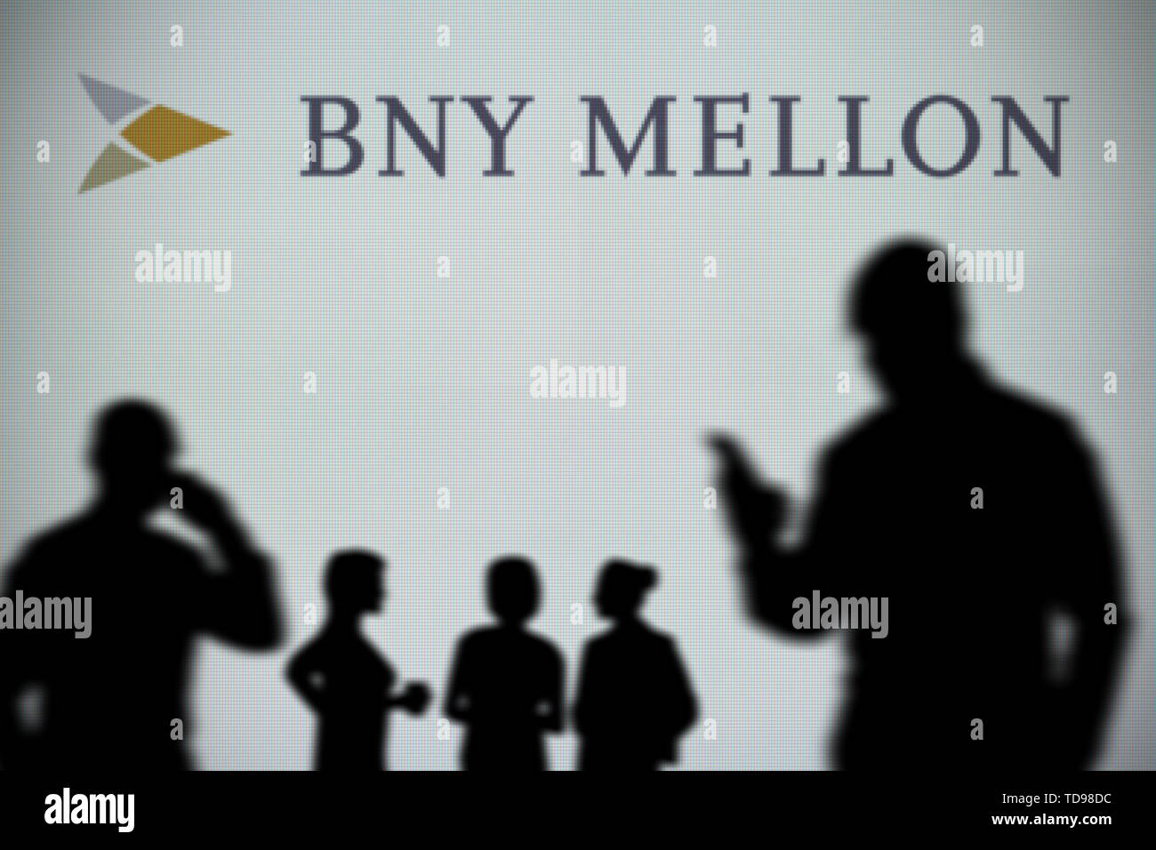 La BNY Mellon logo è visibile su uno schermo a LED in background mentre si profila una persona utilizza uno smartphone in primo piano (solo uso editoriale) Foto Stock