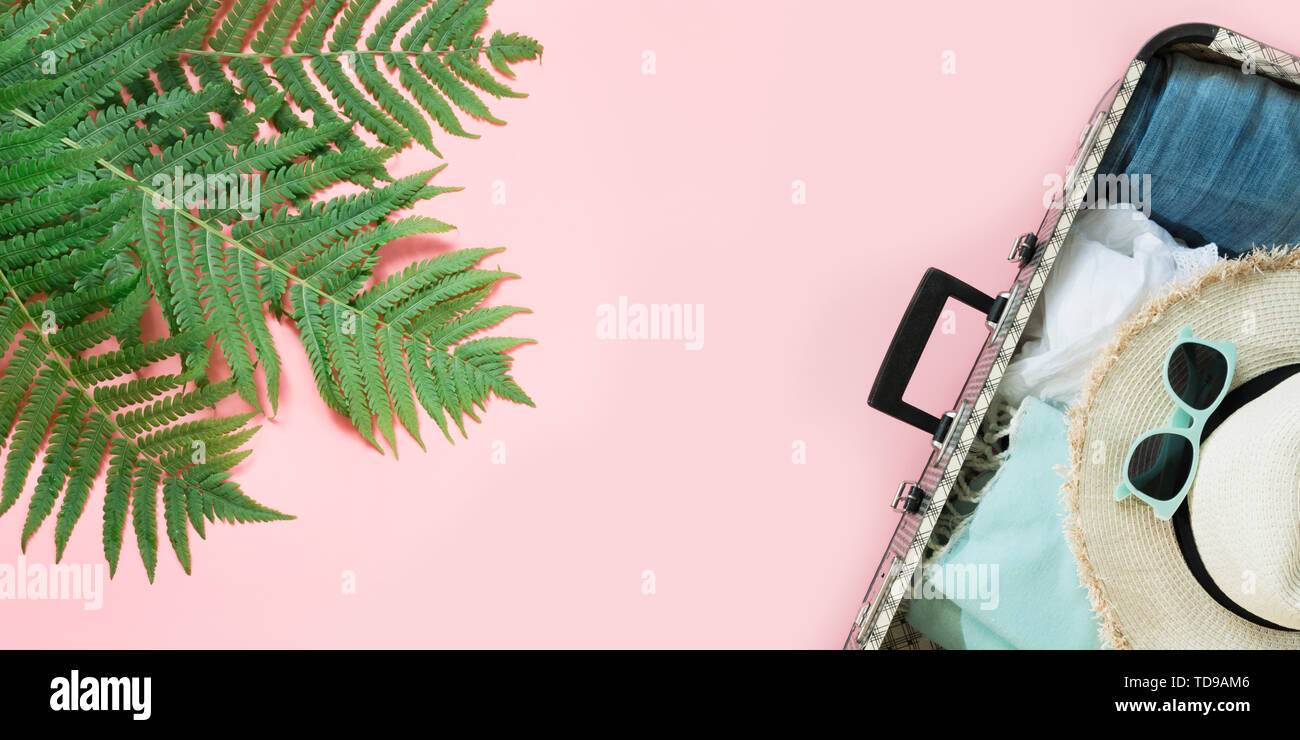 Foglia di felce, tropicale acqua detox e aprire la valigia con vestiti sul rosa pastello sfondo. Vista da sopra con copia spazio. Concetto di estate viaggio. Foto Stock