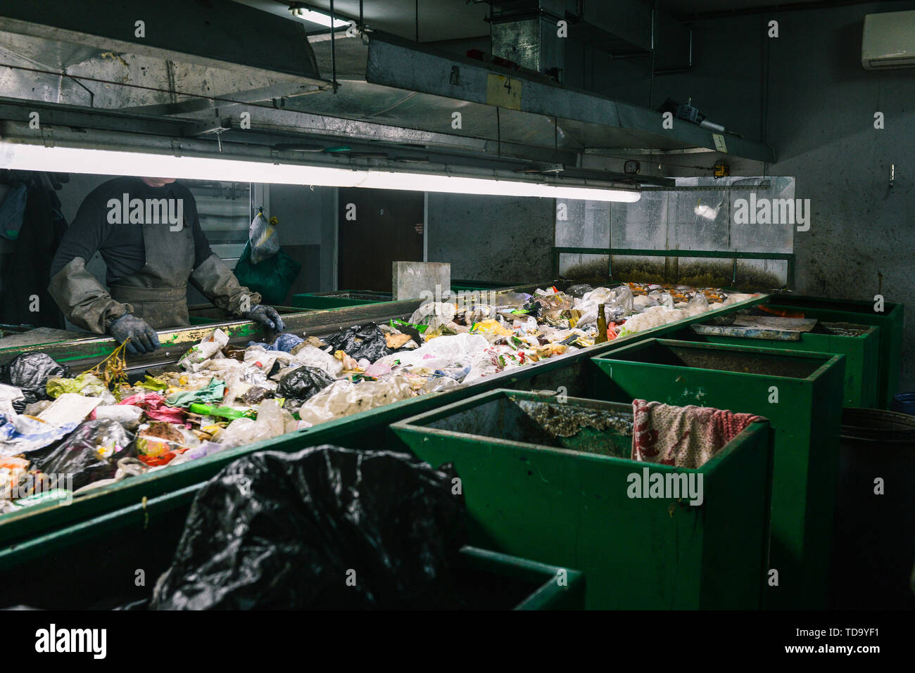 Lavoratore rifiuti impianto di smistamento. Ordinare i rifiuti. Contenitore di rifiuti. Uomo in guanti e grembiuli Foto Stock