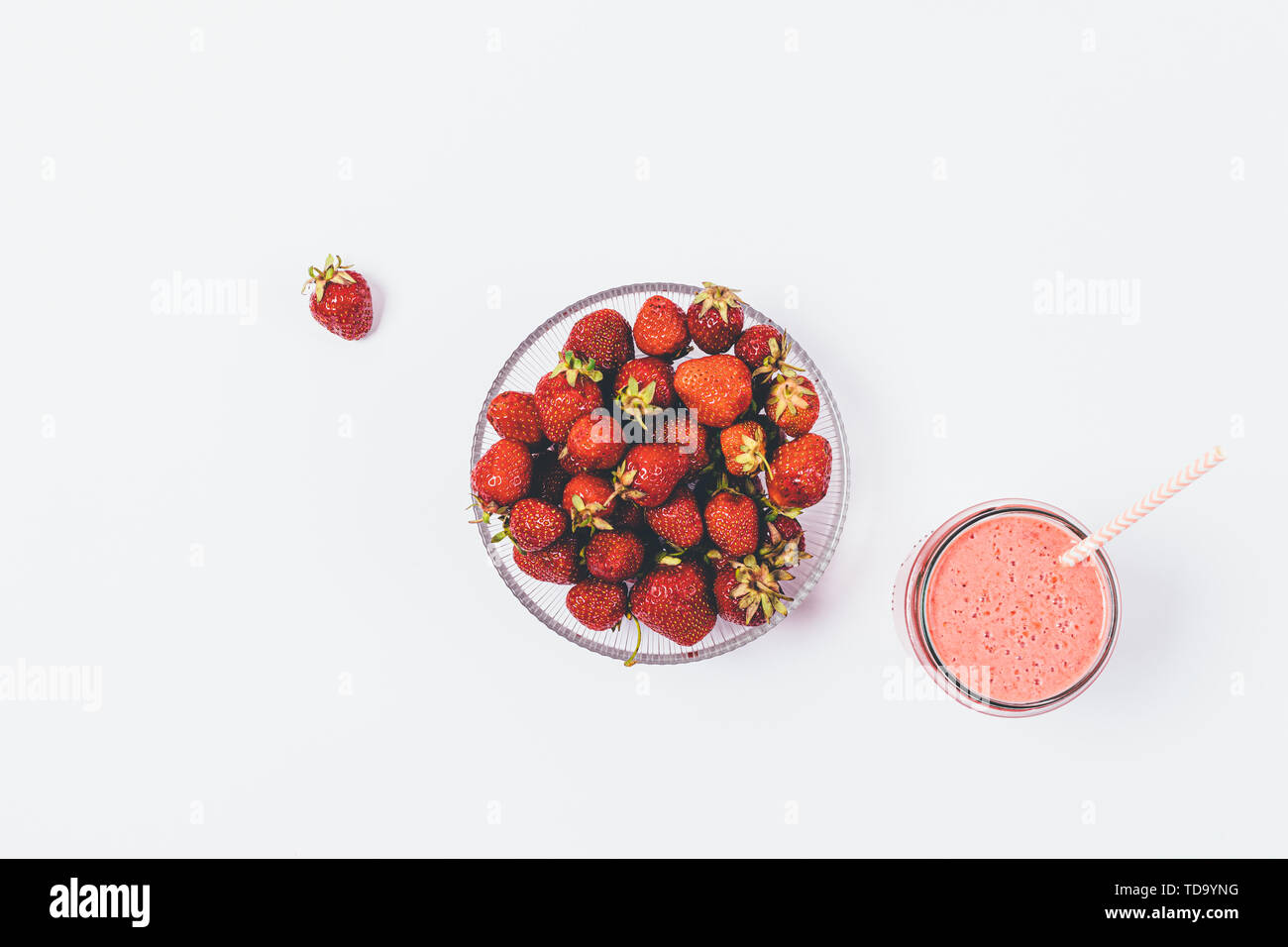 Ciotola piena di fragole fresche accanto al vetro di smoothie su sfondo bianco, piatto laici. Foto Stock