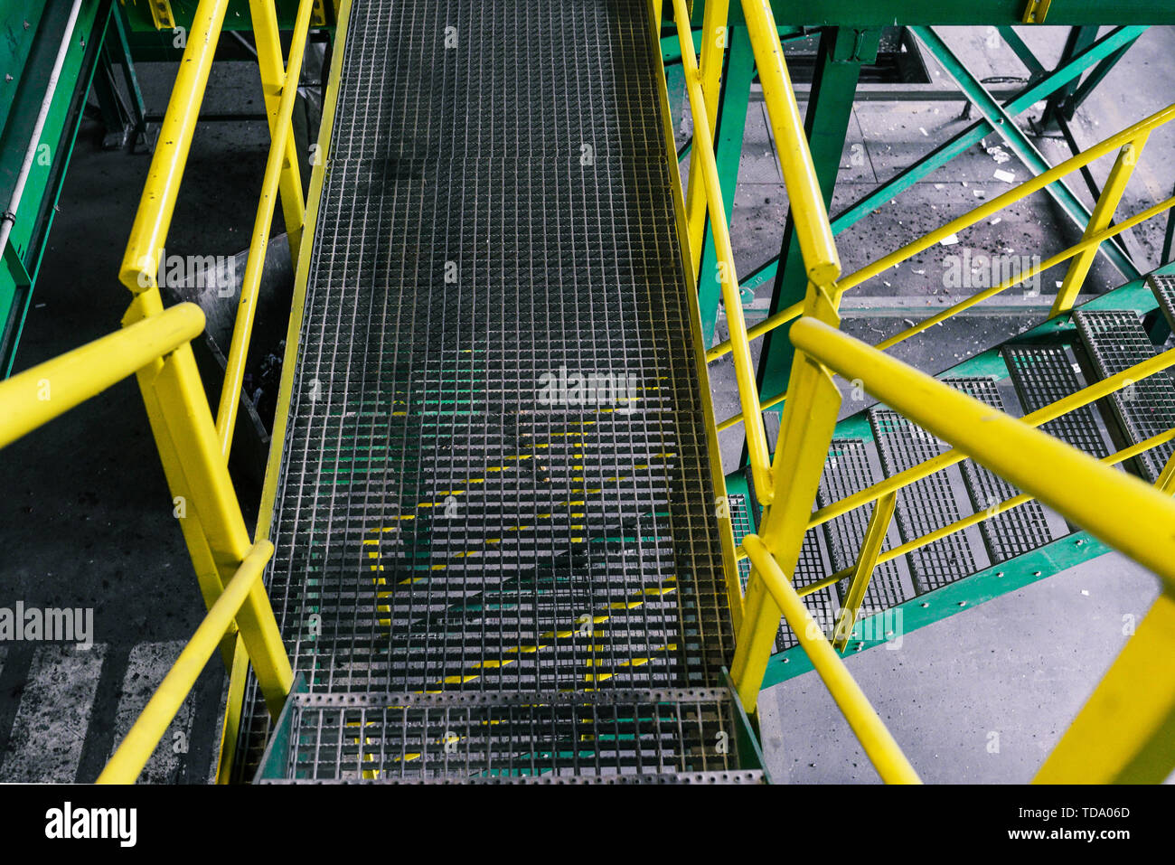 La scala metallica dipinta in colori verde e giallo. Scala di ferro in un impianto industriale o di fabbrica. Reticolo metallico sul pavimento Foto Stock