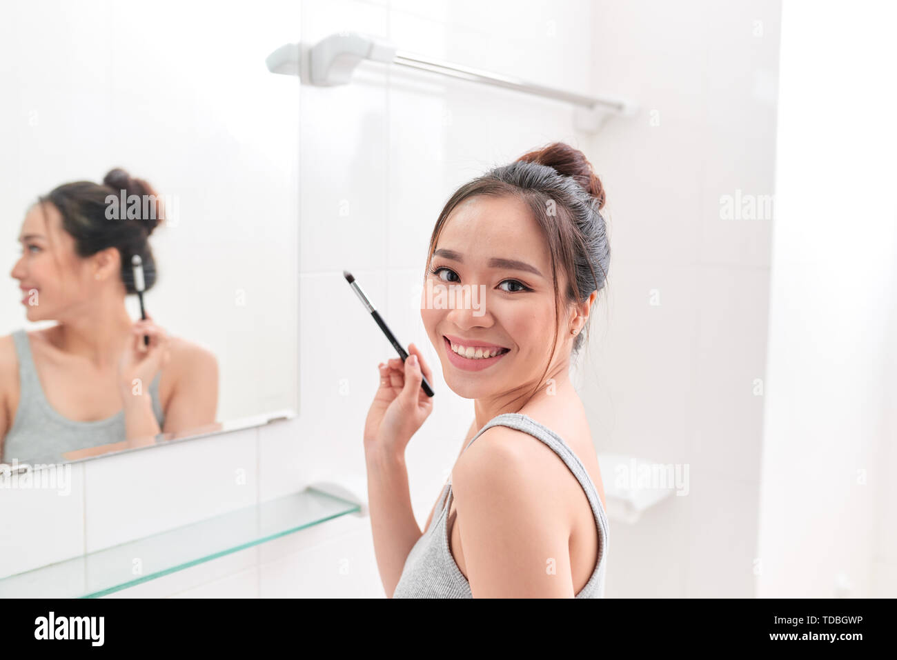 Una giovane donna è in piedi di fronte a specchio del bagno e mettendo il trucco. Foto Stock