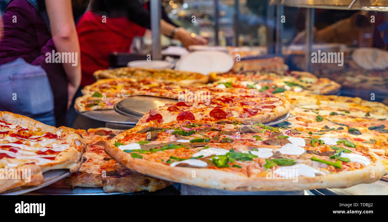 Pizzeria La finestra di vetro. Varietà di pizze italiane in un negozio di display, cibo di strada. Cucina lavoratori disponendo le pizze. Foto Stock