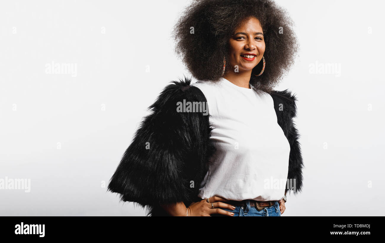 Donna sorridente in acconciatura afro in piedi contro uno sfondo bianco. Ritratto di donna allegra in pelliccia guardando la fotocamera. Foto Stock