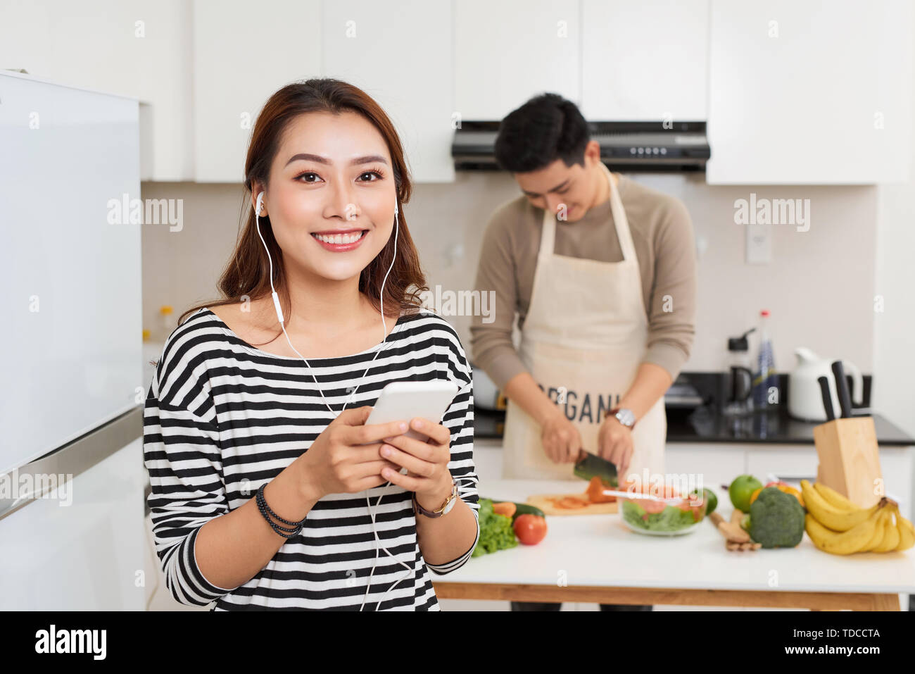 Bella coppia Giovane è la cottura nella cucina di casa.Man è la cottura con Moman è utilizzando una tavoletta digitale e sorridente. Foto Stock