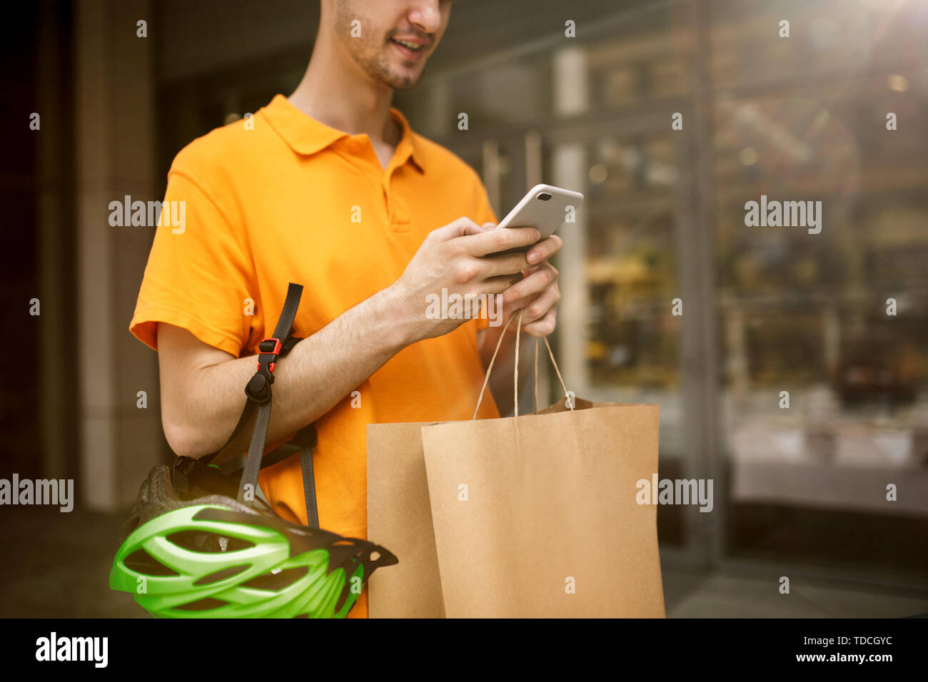 Giovane uomo in maglietta gialla erogazione di pacchetto utilizzando i gadget per via ordine presso la città della strada. Corriere on-line utilizzando app per ricevere il pagamento e il tracking spedizioni indirizzo. Le moderne tecnologie. Foto Stock