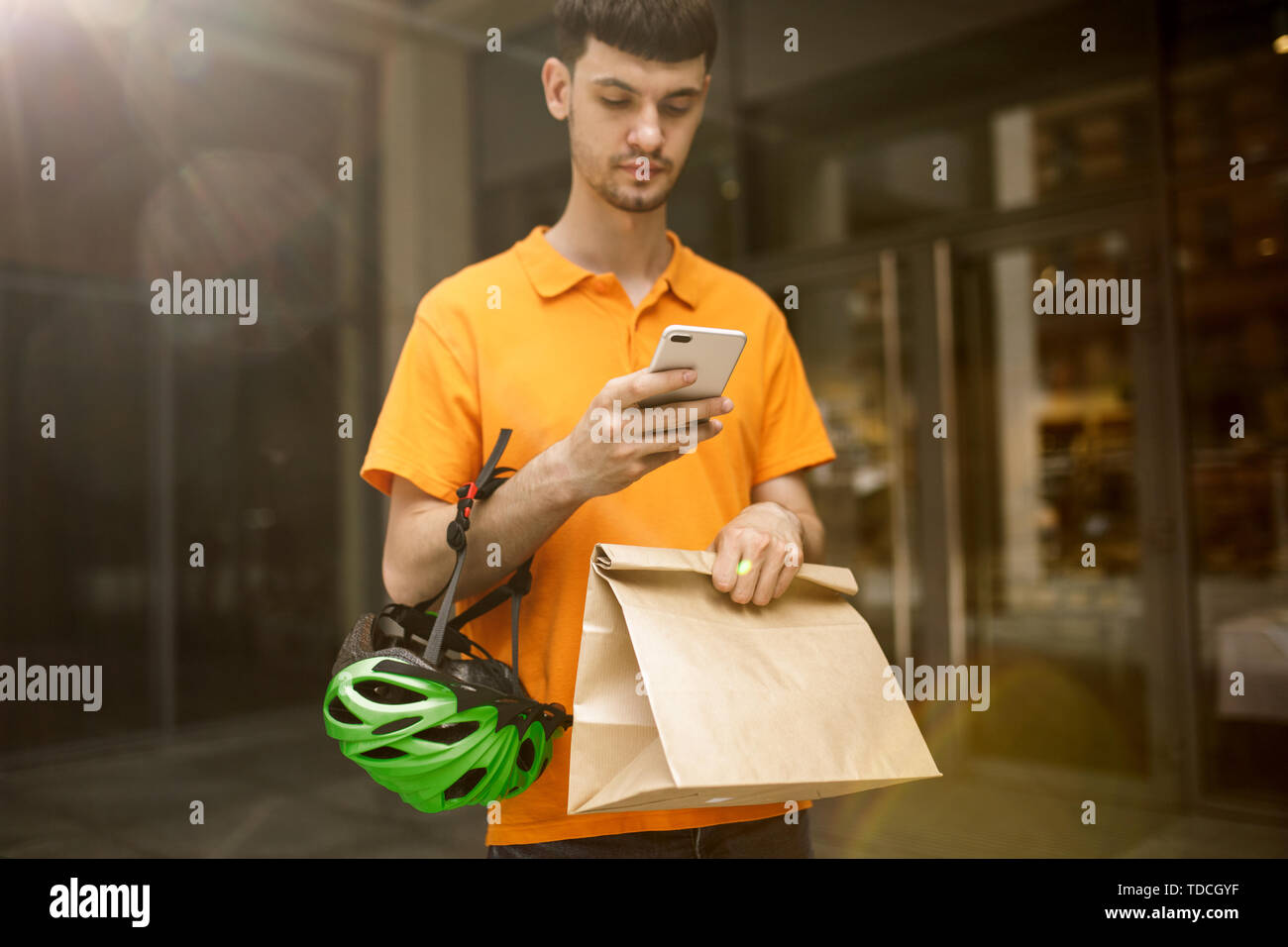 Giovane uomo in maglietta gialla erogazione di pacchetto utilizzando i gadget per via ordine presso la città della strada. Corriere on-line utilizzando app per ricevere il pagamento e il tracking spedizioni indirizzo. Le moderne tecnologie. Foto Stock