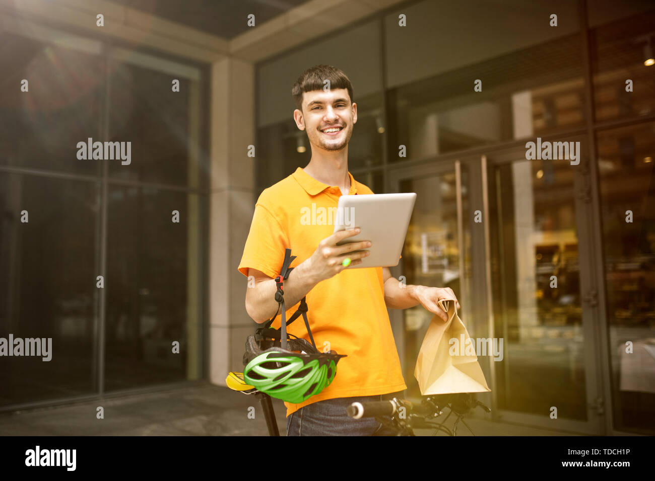 Giovane uomo in maglietta gialla erogazione di pacchetto utilizzando i gadget per via ordine presso la città della strada. Corriere on-line utilizzando app per ricevere il pagamento e il tracking spedizioni indirizzo. Le moderne tecnologie. Foto Stock