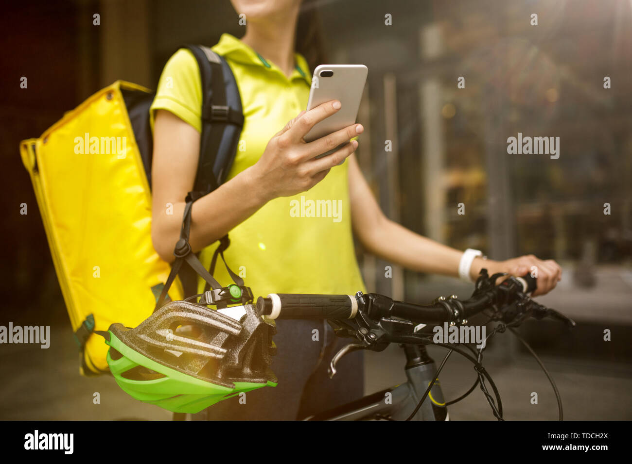 Giovane donna in maglia gialla a consegnare il cibo utilizzando i gadget per via ordine presso la città della strada. Corriere on-line utilizzando app per ricevere il pagamento e il tracking spedizioni indirizzo. Le moderne tecnologie. Foto Stock