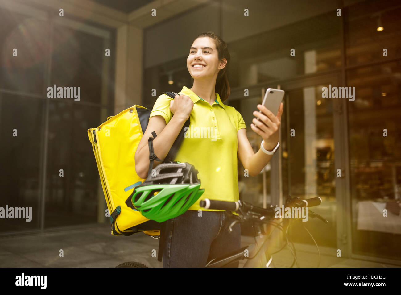 Giovane donna in maglia gialla a consegnare il cibo utilizzando i gadget per via ordine presso la città della strada. Corriere on-line utilizzando app per ricevere il pagamento e il tracking spedizioni indirizzo. Le moderne tecnologie. Foto Stock