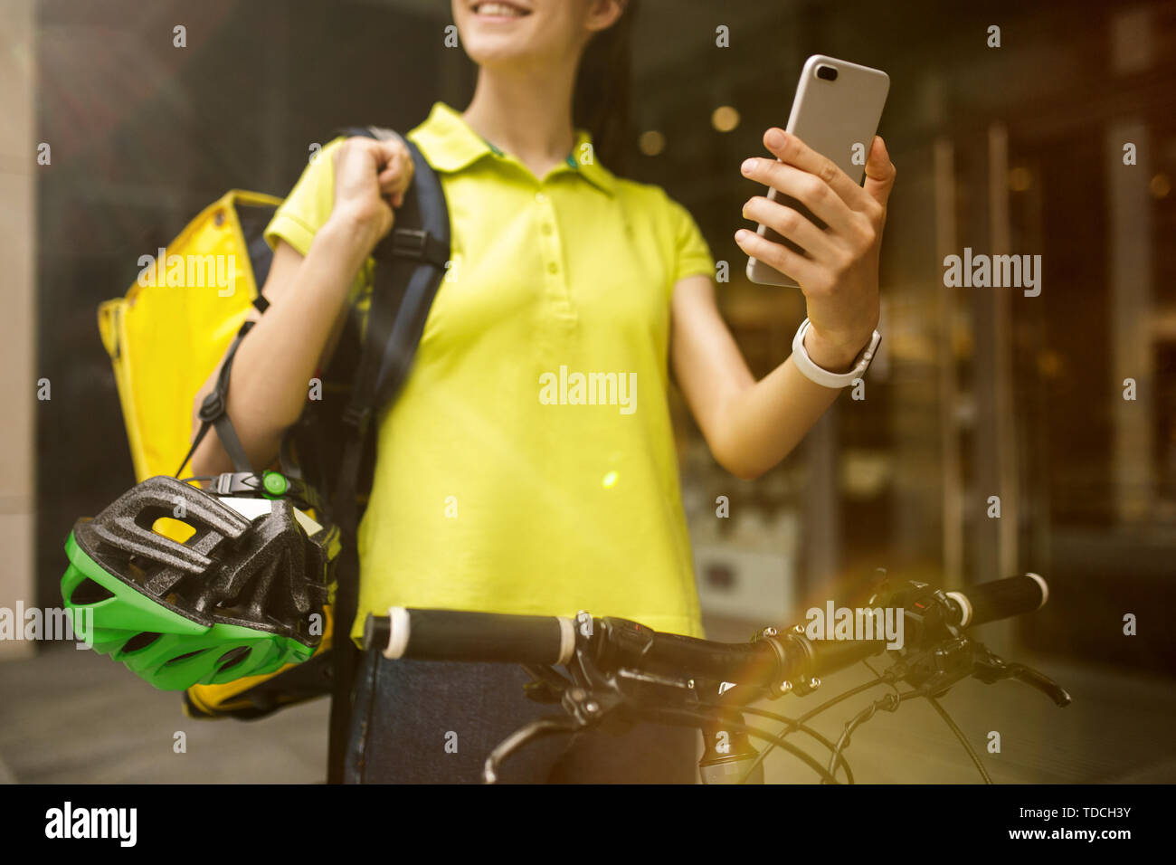 Giovane donna in maglia gialla a consegnare il cibo utilizzando i gadget per via ordine presso la città della strada. Corriere on-line utilizzando app per ricevere il pagamento e il tracking spedizioni indirizzo. Le moderne tecnologie. Foto Stock
