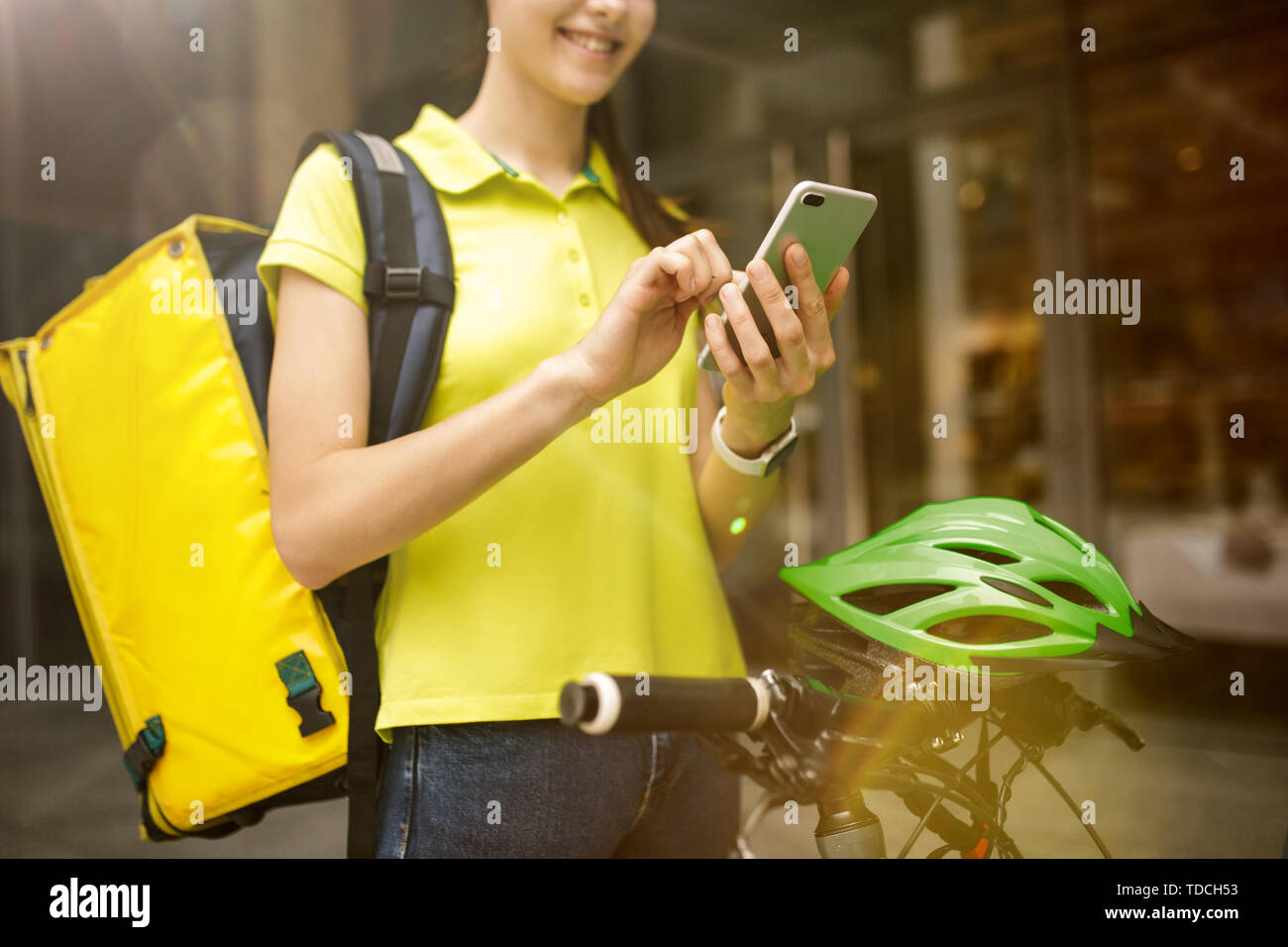 Giovane donna in maglia gialla a consegnare il cibo utilizzando i gadget per via ordine presso la città della strada. Corriere on-line utilizzando app per ricevere il pagamento e il tracking spedizioni indirizzo. Le moderne tecnologie. Foto Stock
