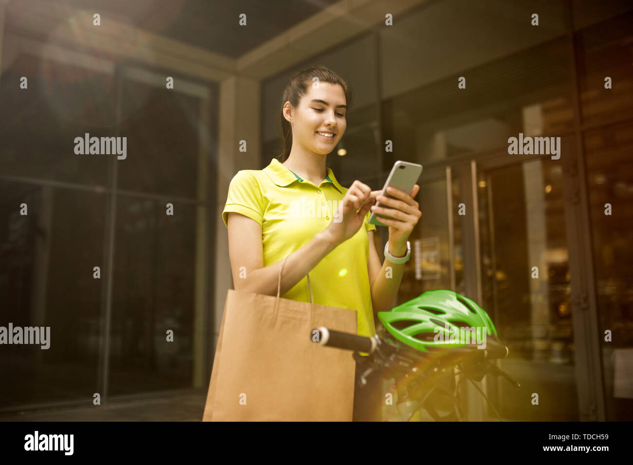 Giovane donna in maglia gialla erogazione di pacchetto utilizzando i gadget per via ordine presso la città della strada. Corriere on-line utilizzando app per ricevere il pagamento e il tracking spedizioni indirizzo. Le moderne tecnologie. Foto Stock